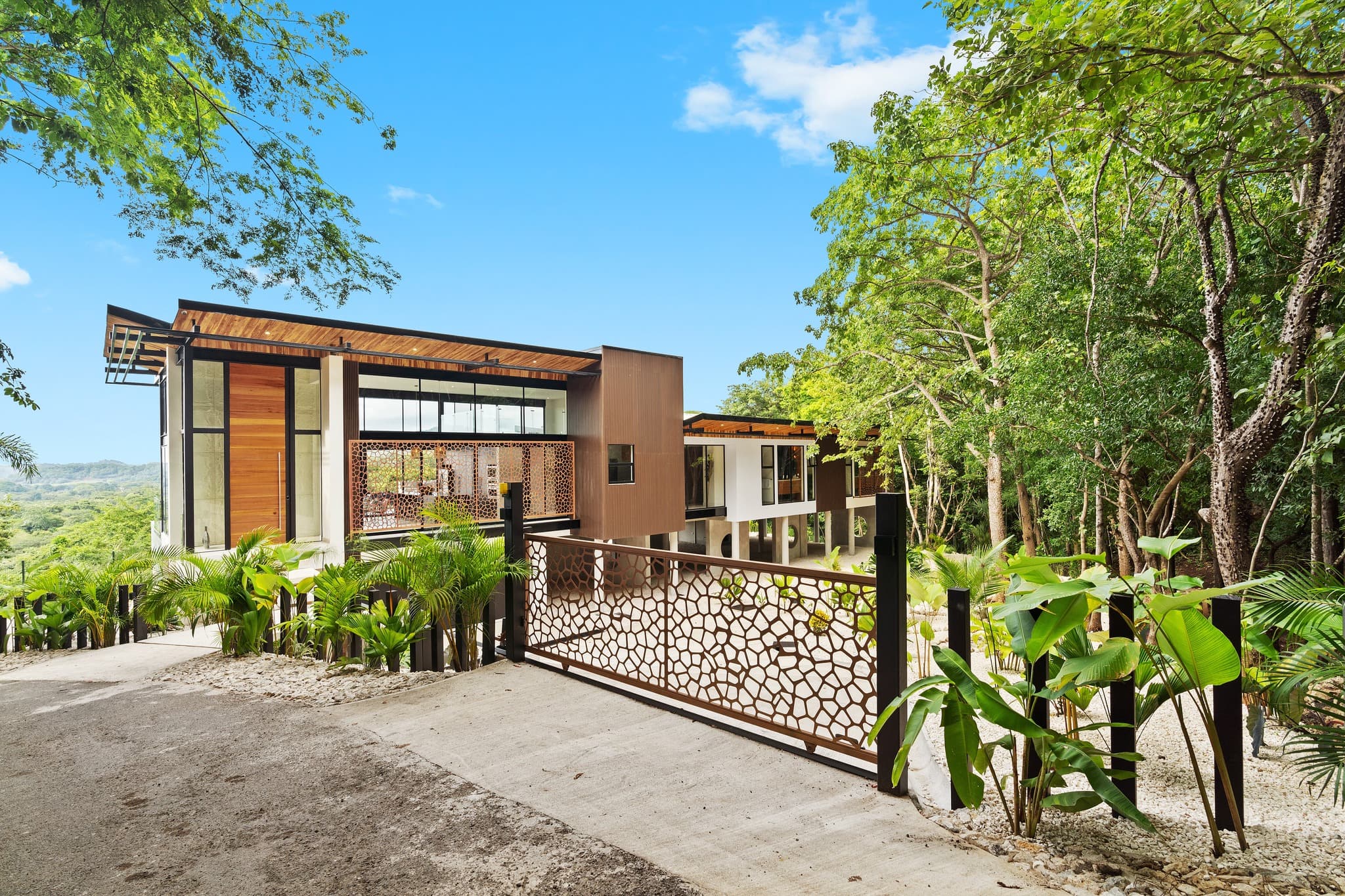 Casa de madera, vidrio y concreto elevada entre el bosque tropical, con portón de celosía de acero corten, diseñada por Habitante Arquitectura